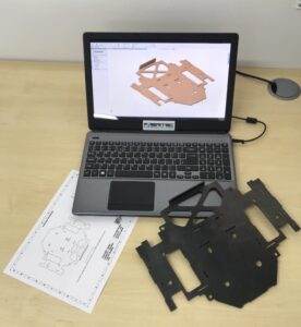 A laptop with a CAD design showing on the screen, with the finished item made from steel.