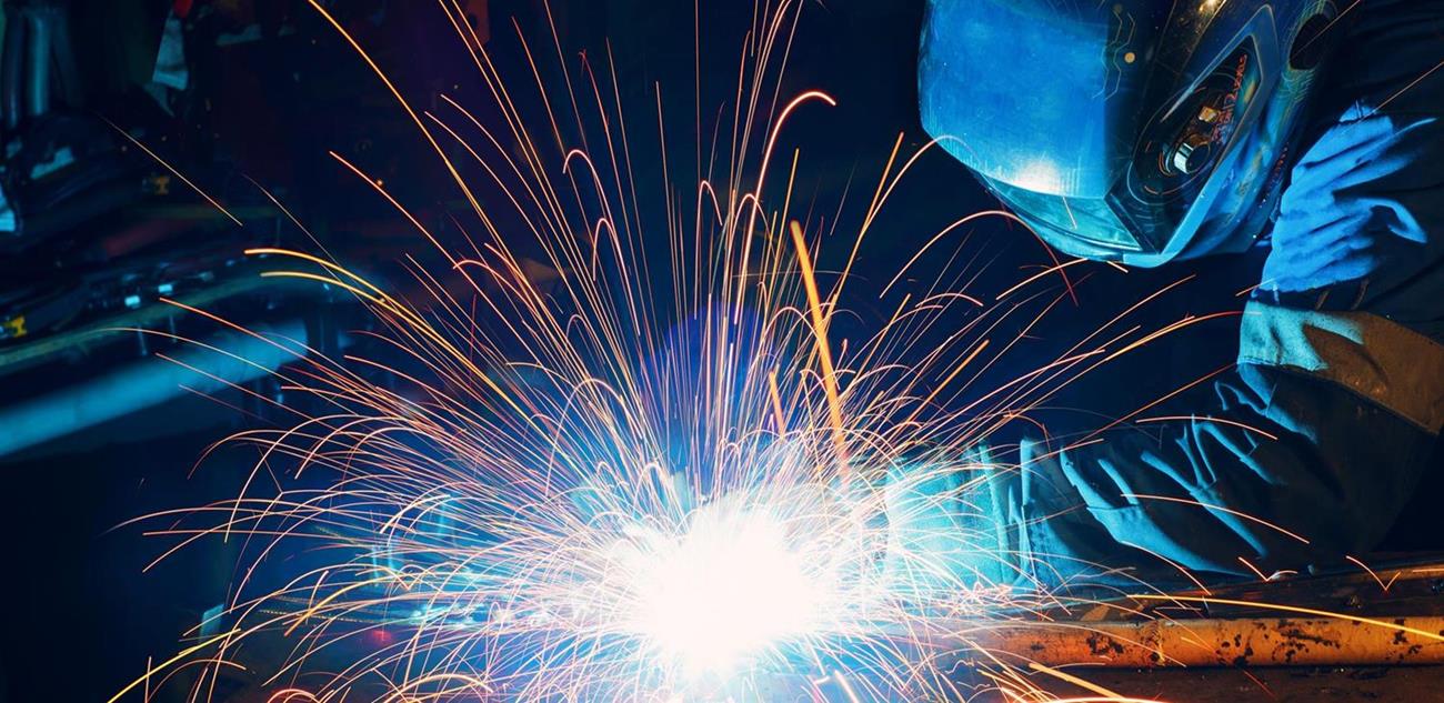 Welder welding metal construction on factory. Long traces of sparks
